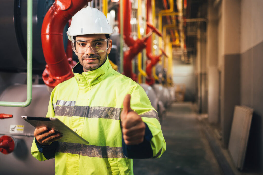 Industriarbetare i skyddsutrustning håller en surfplatta och ger tummen upp i en fabrik